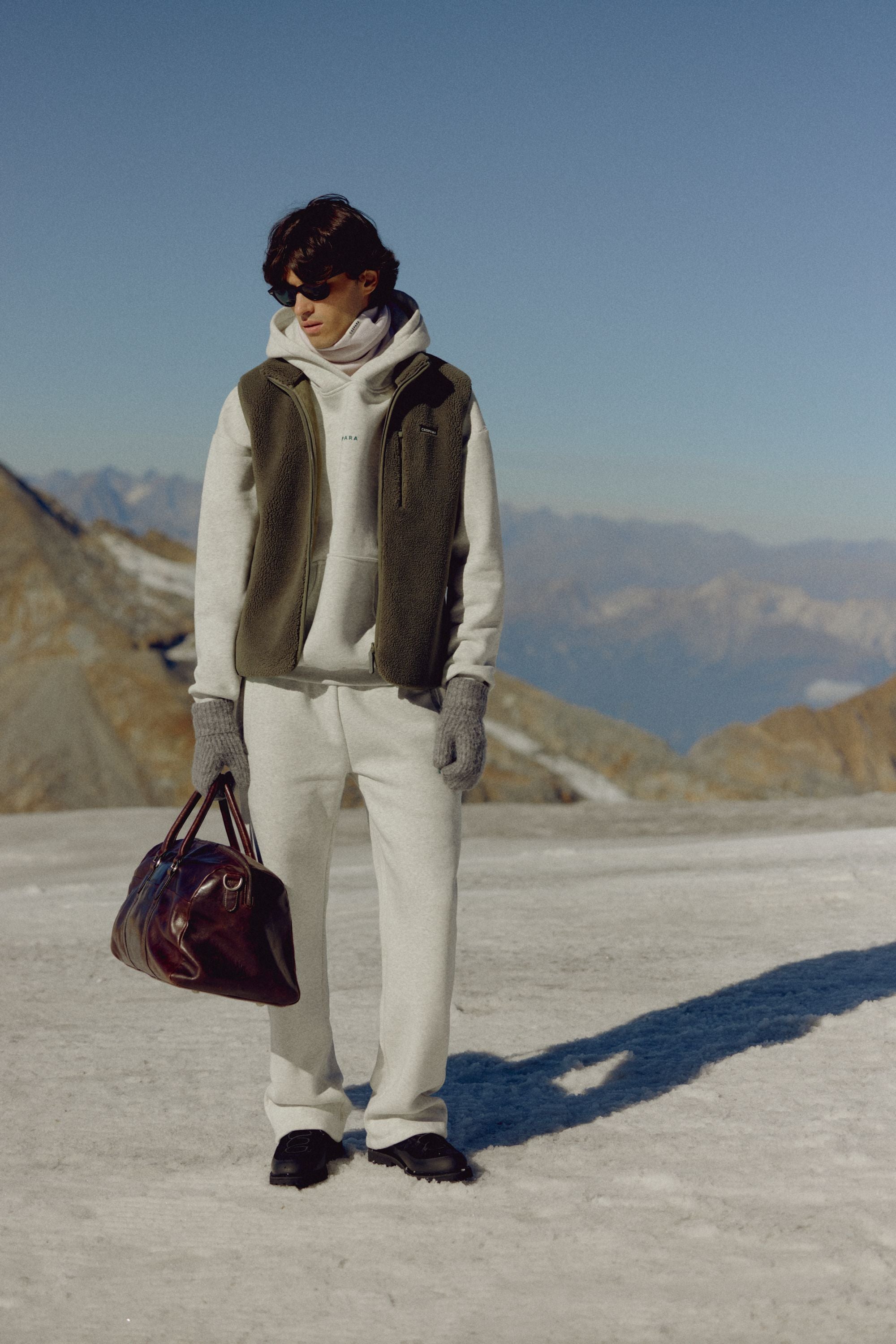 Man wearing a khaki CASPARA Cloudfleece vest standing on snow in a mountain landscape.